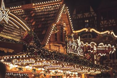 Traditionelle hölzerne Weihnachtsmarkt-Stände geschmückt mit warmen Lichtern und Girlanden. Schilder werben für Schokoladenfrüchte und Süßwaren.