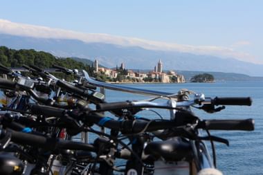Fahrräder mit Blick auf Rab in der Kvarner Bucht Reihe geparkter Fahrräder im Vordergrund mit Blick auf die historische Stadt Rab auf einer Halbinsel in der Kvarner Bucht, Kirchtürme und Berge sichtbar.