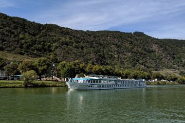 White river cruise ship Switzerland sailing on calm green water with forested hills and small village in the background under blue sky.
