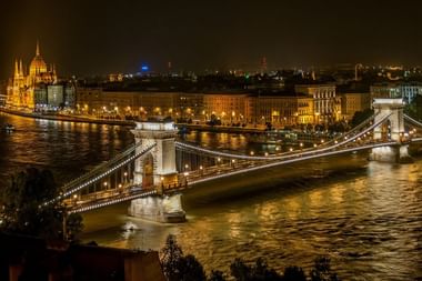 Nachtansicht der beleuchteten Kettenbrücke über die Donau in Budapest mit dem ungarischen Parlamentsgebäude und historischer Uferpromenade.