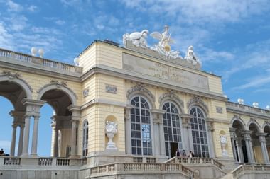 Die Gloriette von Schloss Schönbrunn in Wien, eine neoklassizistische Kolonnade mit Bögen und verzierten Skulpturen auf dem Dach vor blauem Himmel.