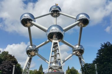 Das Atomium in Brüssel, eine metallische Struktur mit neun verbundenen Kugeln, die ein Eisenkristall darstellt, vor blauem Himmel mit Wolken.