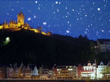 Reichsburg Cochem bei Nacht mit Schnee Beleuchtete Reichsburg auf dem Hügel über bunten Fachwerkhäusern an der Mosel in Cochem bei Schneefall in der Nacht.