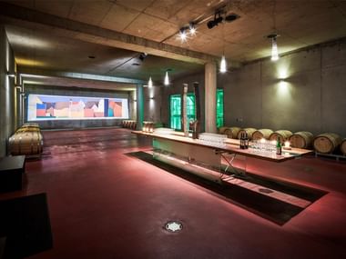 Modern wine cellar in Krems with wooden barrels, concrete walls, pendant lighting, and a tasting table with wine glasses.
