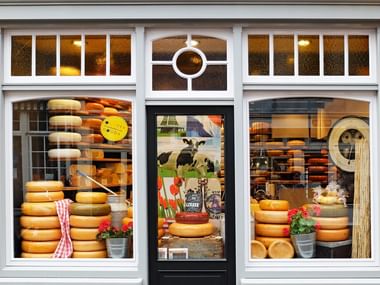 Radfahren in Holland Schaufenster eines Käsegeschäfts in Gouda mit großen Fenstern, die Stapel gelber Käselaibe und holländische Dekorationen zeigen.