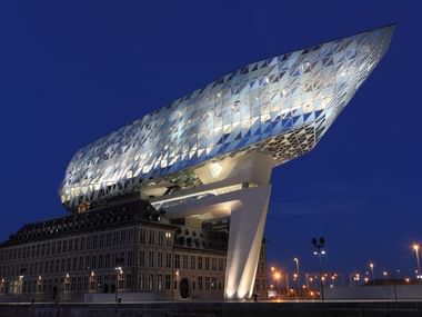 Modern Antwerp Port House at twilight The striking Antwerp Port House building at twilight, featuring a diamond-shaped glass structure on top of a historic brick base against a deep blue sky.