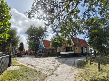 Traditionelle niederländische Häuser mit roten Ziegeldächern im Zuiderzeemuseum in Enkhuizen. Kopfsteinpflasterweg zwischen bunten Gebäuden unter hohen Bäumen.