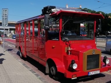 Roter Oldtimer-Touristenbus mit offenen Seiten und slowakischem Kennzeichen auf einer Straße in Bratislava unter blauem Himmel.