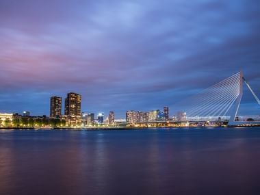 Rotterdam skyline at night with Erasmus Bridge Rotterdam skyline at twilight with illuminated skyscrapers and the iconic white Erasmus Bridge spanning the Nieuwe Maas river.