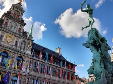 Grote Markt Platz in Antwerpen mit Statue Historischer Grote Markt Platz in Antwerpen mit verzierten Gildenhäusern mit bunten Flaggen und einer Bronzestatue einer Hand werfenden Figur.