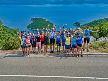 Radlergruppe feiert in Süddalmatien Große Radlergruppe in bunter Radkleidung winkt und feiert auf einer Küstenstraße in Süddalmatien mit blauem Meer und grünen Inseln.