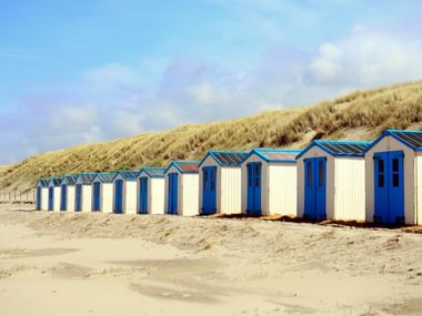Strandhäuser auf Texel Dünen Reihe von weiß-blauen Strandhäusern am Sandstrand mit grasbewachsenen Dünen im Hintergrund unter bewölktem Himmel auf Texel.