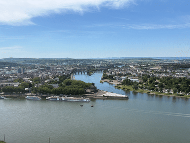 Luftaufnahme von Koblenz mit dem Zusammenfluss zweier Flüsse, Kreuzfahrtschiffen am Ufer und der Stadt im Hintergrund.