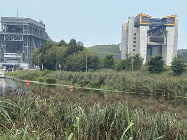 Altes und neues Schiffshebewerk Niederfinow neben einem Kanal mit Schilf. Die historische Stahlkonstruktion steht links, der moderne Betonturm rechts.