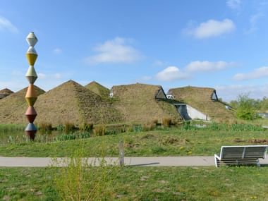 Modern Biesbosch MuseumEiland building with extensive grass-covered roof and colorful sculptural pole in foreground under blue sky.