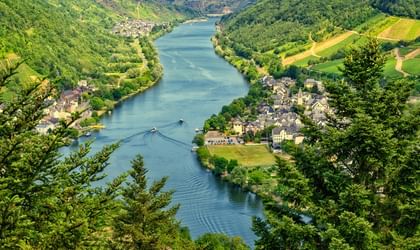 Luftaufnahme eines gewundenen Flusses durch grüne deutsche Landschaft mit einem kleinen Dorf am Ufer, umgeben von bewaldeten Hügeln.