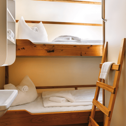 Compact ship cabin on Mare Frisium with wooden bunk beds, white linens, towels, wooden ladder, sink, and storage shelves.