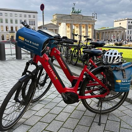 Red and yellow rental bikes parked on cobblestones with Brandenburg Gate visible in the background under a cloudy sky in Berlin.