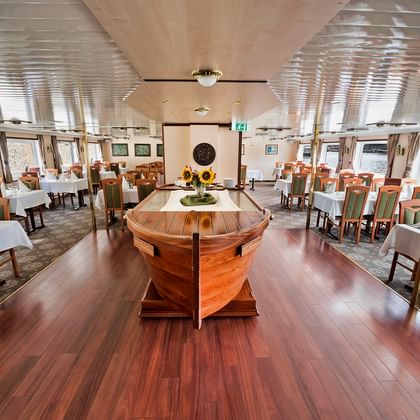 Innenraum des MS Florentina Restaurants mit bootförmigem Holzbuffet, weißen Tischdecken, grünen Stühlen und Panoramafenstern.