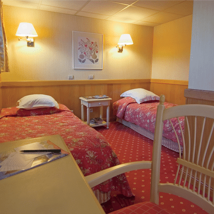 Gemütliche Kabine auf dem Schiff Provence mit zwei Einzelbetten, rot gemusterten Tagesdecken, Holzverkleidung, Wandlampen und kleinem Schreibtisch.