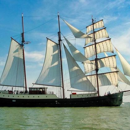 Dreimastiges Segelschiff Simmer Fan Fryslân mit weißen Segeln auf ruhigem Wasser unter blauem Himmel mit Wolken.