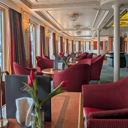 Elegant salon on the Casanova ship with red upholstered chairs, round tables with tulips, large windows, white columns, and decorative ceiling.