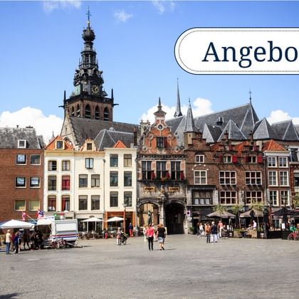 Historischer Marktplatz mit bunten niederländischen Häusern und Kirchturm. Menschen flanieren über den Platz unter blauem Himmel.