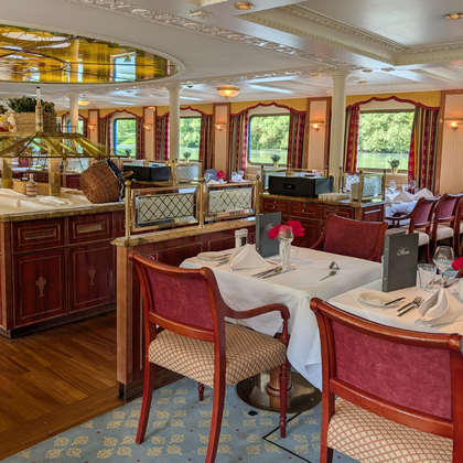 Elegantes Restaurant an Bord der Casanova mit burgunderroten Polsterstühlen, weiß gedeckten Tischen, Holzbuffet und großen Fenstern mit Blick aufs Wasser.