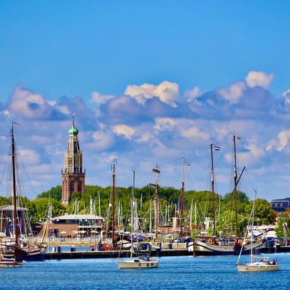 Marina in Enkhuizen mit zahlreichen Segelbooten und Yachten im blauen Wasser. Historischer Kirchturm mit grüner Kuppel ragt über Bäume.