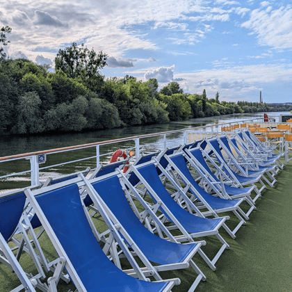 Sun deck of Casanova with rows of blue and white deck chairs along the railing. River with green trees and another ship visible in background.