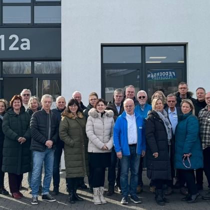 Group of approximately 25 tour guides standing together in front of a modern building entrance marked '12a', dressed in winter clothing.