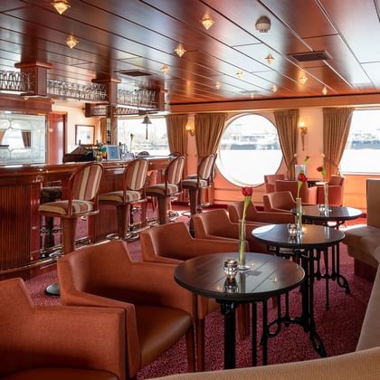 Elegante Salon Bar auf dem Schiff Switzerland mit Holztheke, Ledersesseln, runden Tischen und runden Bullaugen mit Blick aufs Wasser.