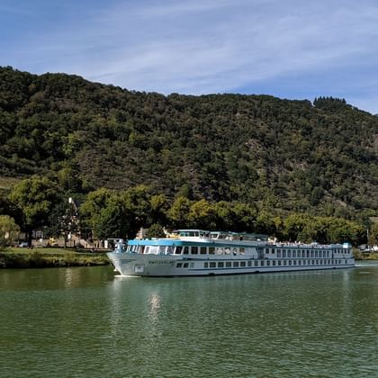 White river cruise ship Switzerland sailing on calm green water with forested hills and small village in the background under blue sky.