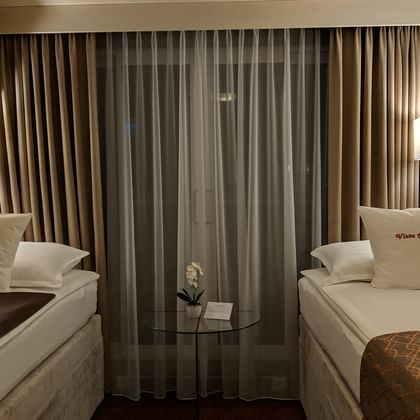 2-Bett-Kabine auf MS Classica mit zwei Betten, beigen Vorhängen, Wandlampen und Zierkissen. Kleiner Tisch mit Orchidee zwischen den Betten.