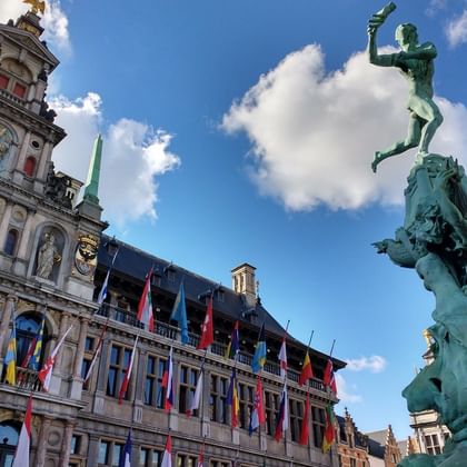 Grote Markt square in Antwerp with statue Historic Grote Markt square in Antwerp featuring ornate guild houses with colorful flags and a bronze statue of a figure throwing a hand.
