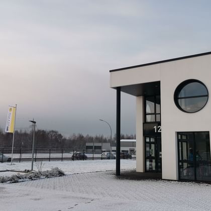 Modernes weißes Bürogebäude mit SE Tours Logo, rundem Fenster und Glaseingang. Schnee bedeckt den Boden und Fahnen stehen im Parkbereich.