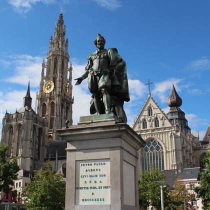 Peter Paul Rubens statue in Antwerp Bronze statue of Peter Paul Rubens on stone pedestal in Antwerp, with Cathedral of Our Lady's Gothic spire in background under blue sky.