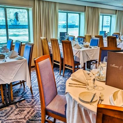 Elegant restaurant on SE Manon with tables set with white linens, wine glasses, and menu cards. Large windows overlook the waterfront.
