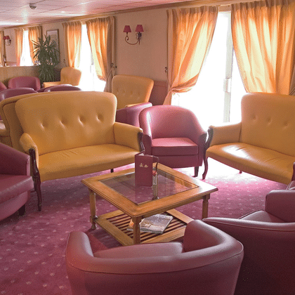Geräumiger Salon auf dem Schiff Provence mit gelben Sofas, rosa Sesseln, Holzcouchtisch, pfirsichfarbenen Vorhängen und rosa Teppich.