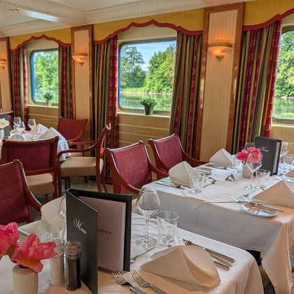 Elegantes Casanova Restaurant-Interieur mit gedeckten Tischen, bordeauxroten Polstermöbeln und großen Fenstern mit Blick auf grüne Flusslandschaft.