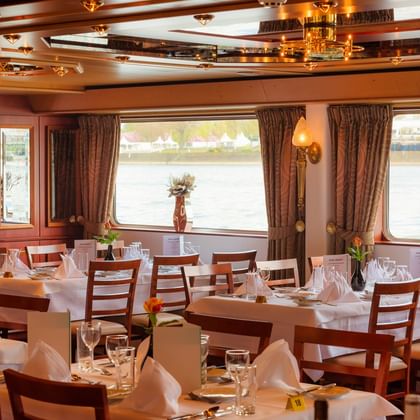 Elegant restaurant aboard MS Switzerland with white-clothed tables, wooden chairs, and large windows overlooking the water.