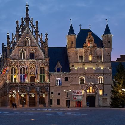 Historische Gebäude am Grote Markt in Antwerpen in der Dämmerung. Verziertes gotisches Rathaus mit beleuchteter Fassade neben mittelalterlichen Gebäuden.