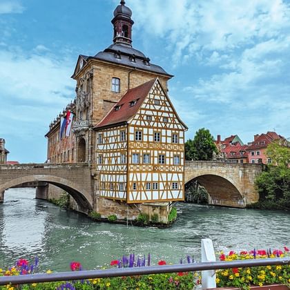 Bamberg's famous Old Town Hall with half-timbered facade built on a bridge over the Regnitz river, surrounded by colorful historic buildings.