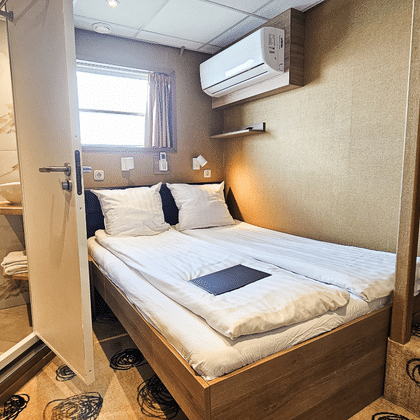 Compact upper deck cabin on MS Nassau with double bed, white linens, ensuite bathroom, window, air conditioning, and patterned carpet.