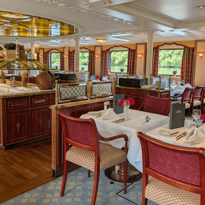 Elegant restaurant aboard Casanova with burgundy upholstered chairs, white-clothed tables, wooden buffet counter, and large windows overlooking water.