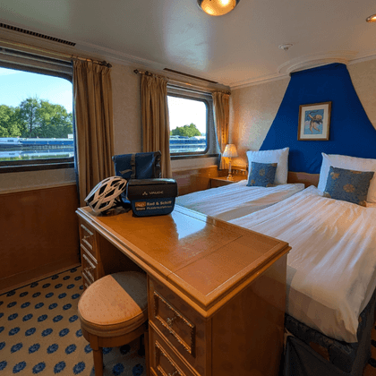 Spacious cabin with double bed, blue accent wall, wooden desk, patterned carpet, and large windows overlooking the river on Casanova ship.