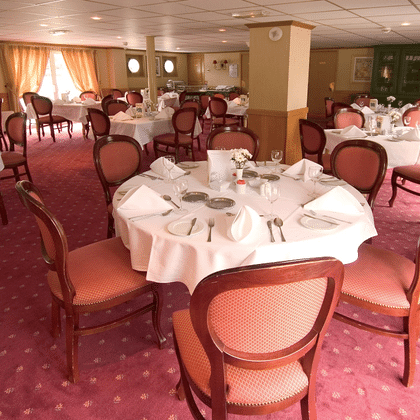 Eleganter Speisesaal auf dem Schiff Provence mit runden Tischen mit weißen Tischdecken, burgunderroten Polsterstühlen und rosa gemustertem Teppich.