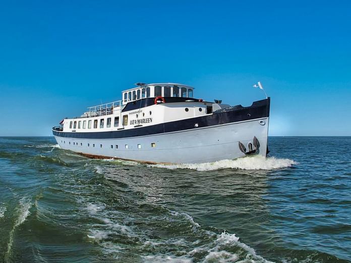 White passenger ship MPS Liza Marleen with black hull cruising through blue-green waters under clear blue sky, creating wake behind.