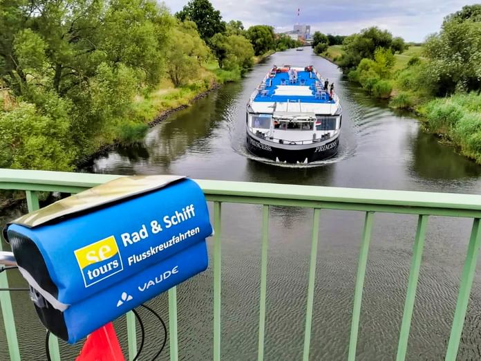 Weißes Passagierschiff MS Princess mit blauem Deck fährt auf der Oder. Blaue Radtour-Tasche mit 'Rad & Schiff' Text an Brückengeländer.