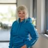 Kerstin Wulfsohn trägt einen blauen Hoodie mit weißem Text am Ärmel und steht in einem modernen Büroflur mit großen Fenstern.